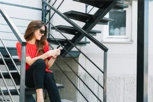 smiling young woman sitting staircase using cellphone 23 2147925320